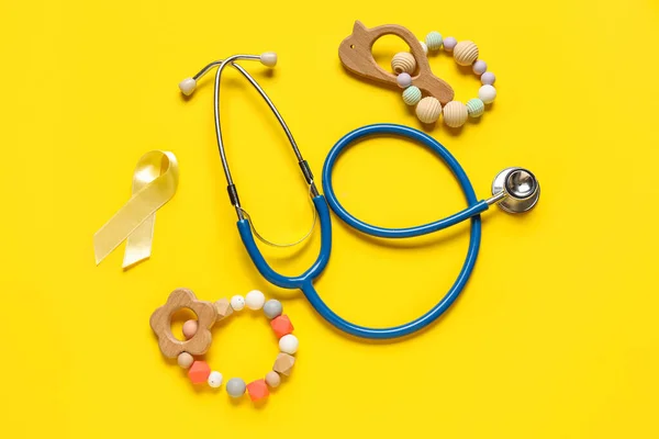 Golden ribbon with rattles and stethoscope on yellow background. Childhood cancer awareness concept