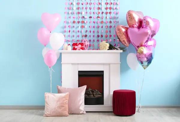 Fireplace with heart-shaped balloons and garland near blue wall. Valentine\'s Day celebration