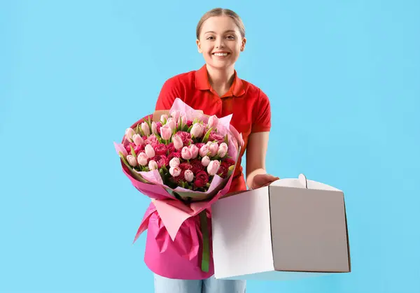 Female courier with bouquet of flowers and box on blue background