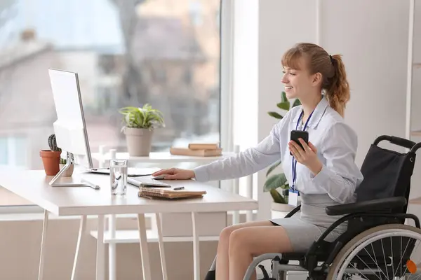 stock image Young businesswoman in wheelchair working with computer and mobile phone at office