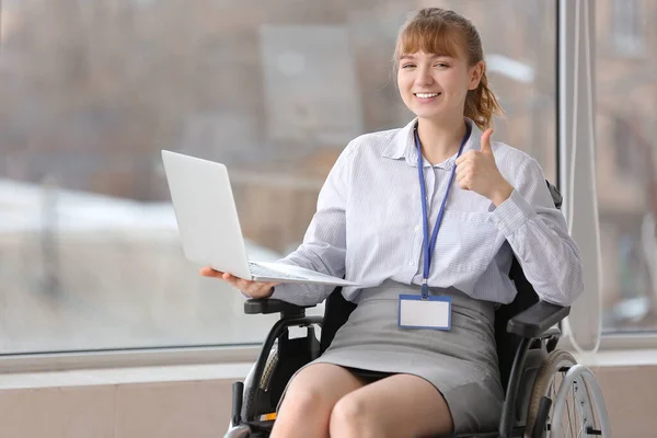 Young businesswoman in wheelchair with laptop showing thumb-up at office