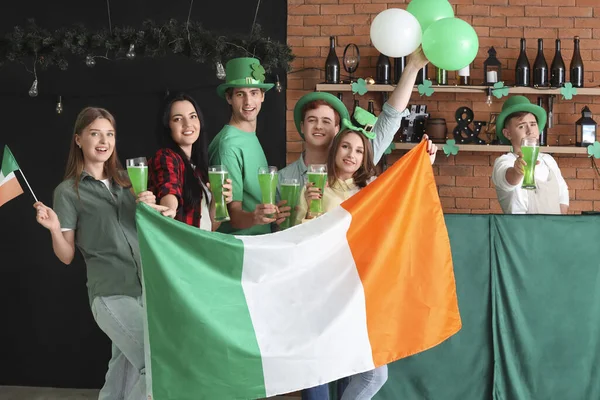 Group of young people with beer and Irish flags celebrating St. Patrick\'s Day in pub