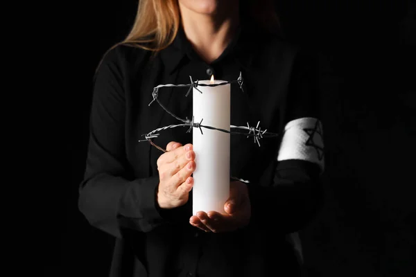 Mature woman with candle and barbed wire on black background, closeup. International Holocaust Remembrance Day