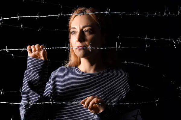 Mature Jewish woman behind barbed wire on black background. International Holocaust Remembrance Day