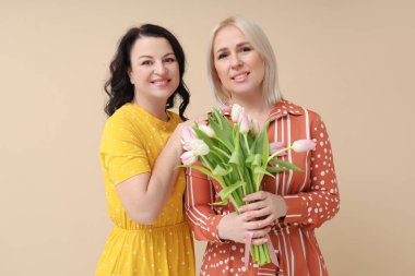 Bej arka planda güzel lalelerle dolu buketi olan mutlu olgun kadınlar. Uluslararası Kadınlar Günü