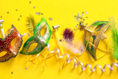 Mardi Gras için sarı arka planda parti kornaları ve dekorları olan karnaval maskeleri.