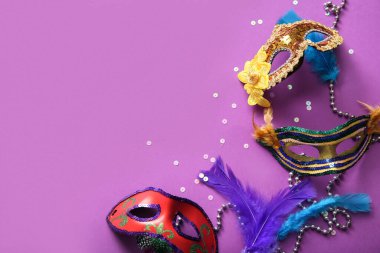 Mardi Gras kutlamaları için tüylü ve boncuklu karnaval maskeleri mor arka planda.