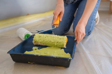 Boyalı silindirli genç bir kadın odada tamirat yapıyor, yakın plan.