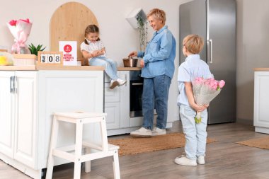 Küçük çocuk mutfakta kız kardeşini ve büyükannesini selamlıyor. Uluslararası Kadınlar Günü