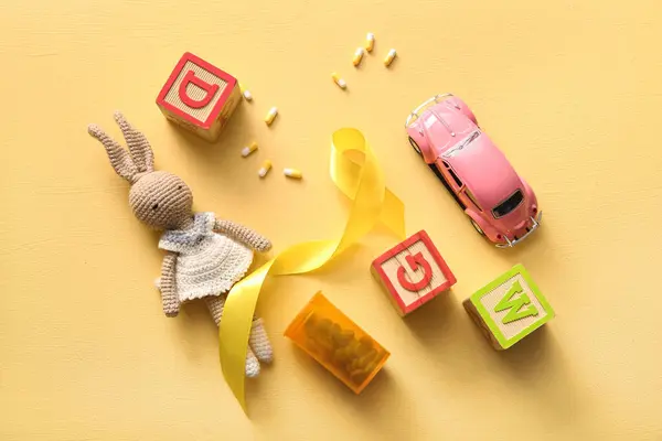 Goldene Schleife Mit Pillen Und Spielzeug Auf Gelbem Hintergrund Kinderkrebsaufklärungskonzept — Stockfoto