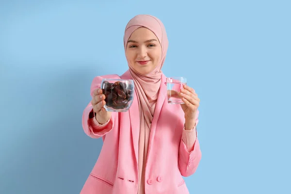 Young Muslim woman with dates and glass of water on blue background. Ramadan celebration