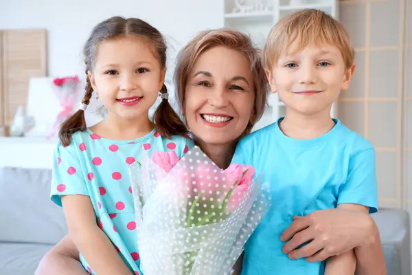 Mature woman with tulips hugging her little grandchildren at home. International Women\'s Day