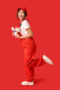 Kırmızı arka planda boya fırçası ve palet örnekleri olan mutlu kadın ressam.