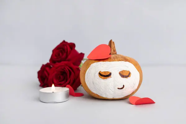 Pumpkin with drawn face, paper hearts, roses and clay mask on grey background