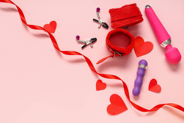 Состав с секс-игрушками и бумажными сердечками на розовом фоне. Празднование Дня Святого Валентина