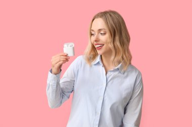 Pembe arka planda kablosuz kulaklıkları olan güzel bir genç kadın.