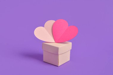 Mor arka planda hediye kutusu olan kağıt kalpler.