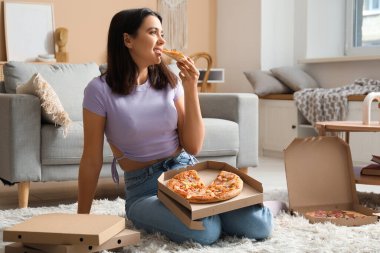 Güzel, genç bir kadın evde lezzetli bir pizza yiyor.