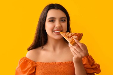 Sarı arka planda lezzetli pizza yiyen genç bir kadın.