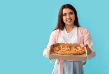 Elinde mavi arka planda lezzetli pizzayla karton kutu tutan genç bir kadın.