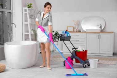 Kadın hademe banyoda yerleri paspaslıyor.