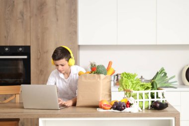 Mutfakta farklı sebzeleri ve modern dizüstü bilgisayarı olan sevimli bir çocuk.