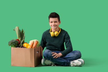 Şirin küçük çocuk ve yeşil arka planda farklı sebzeleri olan karton kutu.