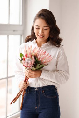 Evinin penceresinin yanında güzel protea çiçekleri olan genç Asyalı kadın.