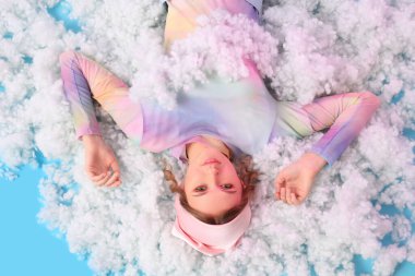 Beyaz bulutların üzerinde uzanan genç kadın mavi arka plan, üst görünüm