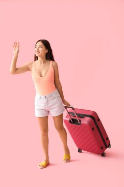 Pembe arka planda bavulu olan mutlu genç kadın.