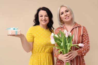 Bir buket güzel lalesi ve bej arka planda hediye kutusu olan olgun kadınlar. Uluslararası Kadınlar Günü