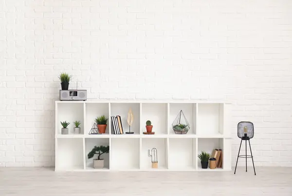 TV stand with books and plants near white brick wall in room