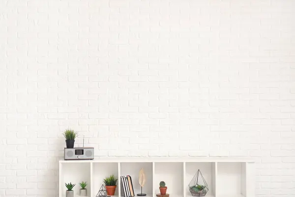 TV stand with books and plants near white brick wall in room