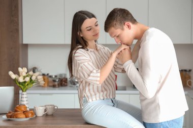 Genç adam mutfakta kız arkadaşının elini öpüyor.