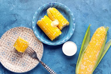 Mavi arka planda tereyağlı haşlanmış mısır koçanı tabakları