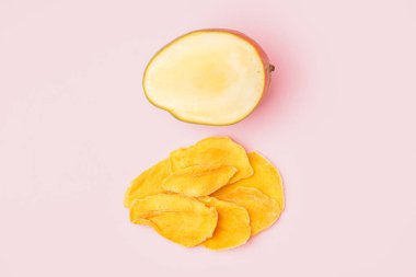 Kurutulmuş mango dilimleri ve pembe masada taze meyve.