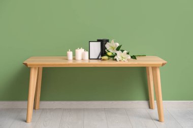 Boş cenaze iskeleti, yanan mumlar ve renkli duvarın yanındaki ahşap masada güzel zambak çiçekleri.