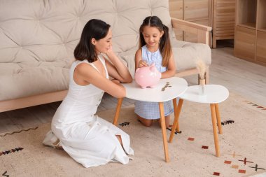 Annesiyle küçük bir kız evdeki kumbaraya para koyuyor.