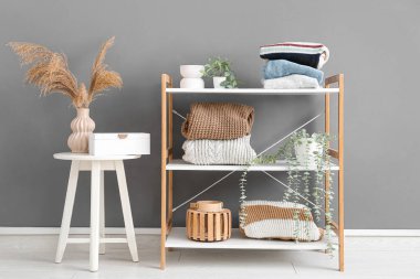 Gri duvarın yanında raf ünitesi, tabure ve şık süveterler olan aydınlatma odasının içinde.