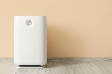 Odada bej duvarın yanında hava temizleyici var.