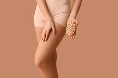 Selülit sorunu ve kahverengi arka planda masaj fırçası olan güzel bir genç kadın.