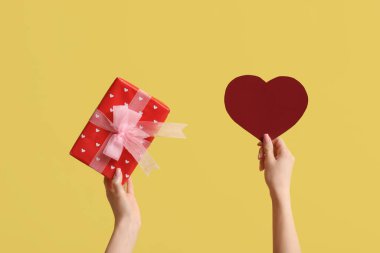 Kağıt kalpli kadın eller ve sarı arka planda hediye kutusu. Sevgililer Günü kutlaması