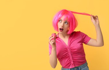 Pembe peruklu güzel bir kadın sarı arka planda tatlı badem kurabiyesi yiyor.