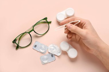 Cımbız, gözlük ve kontakt lensler için bej arka planda bulunan kadın eli.