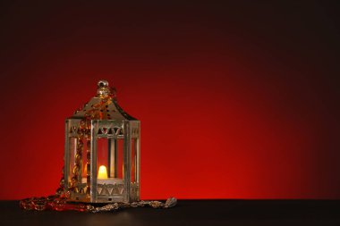 Ramazan için yanan mum ve tespih taşıyan Müslüman lambası koyu kırmızı arka planda.