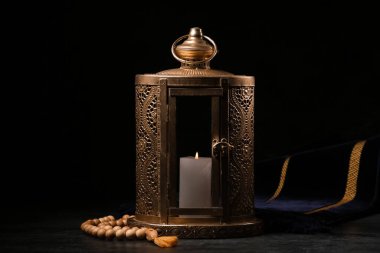 Ramazan ayı için yanan mum ve tespih taşıyan Müslüman feneri koyu arkaplanda.