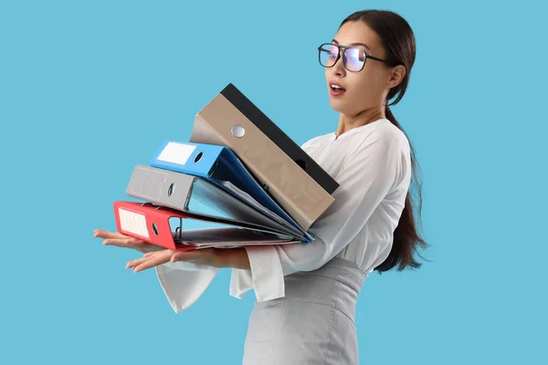 Stressed Asian businesswoman with document folders on blue background