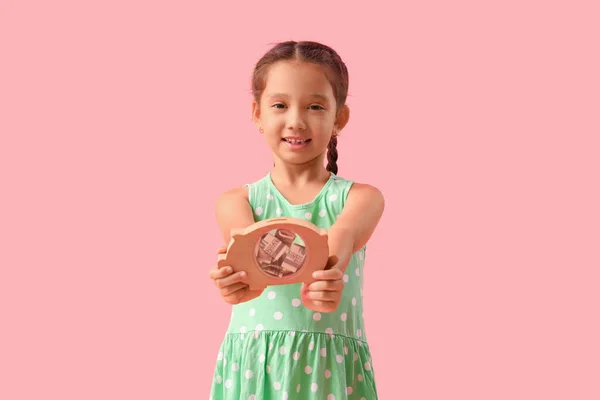 有粉色背景的小猪银行的小女孩 — 图库照片