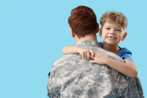 Little boy hugging his military father on blue background, closeup