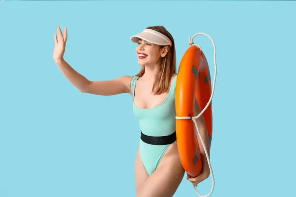 stock image Beautiful young woman in tank swimsuit and with lifebuoy on blue background